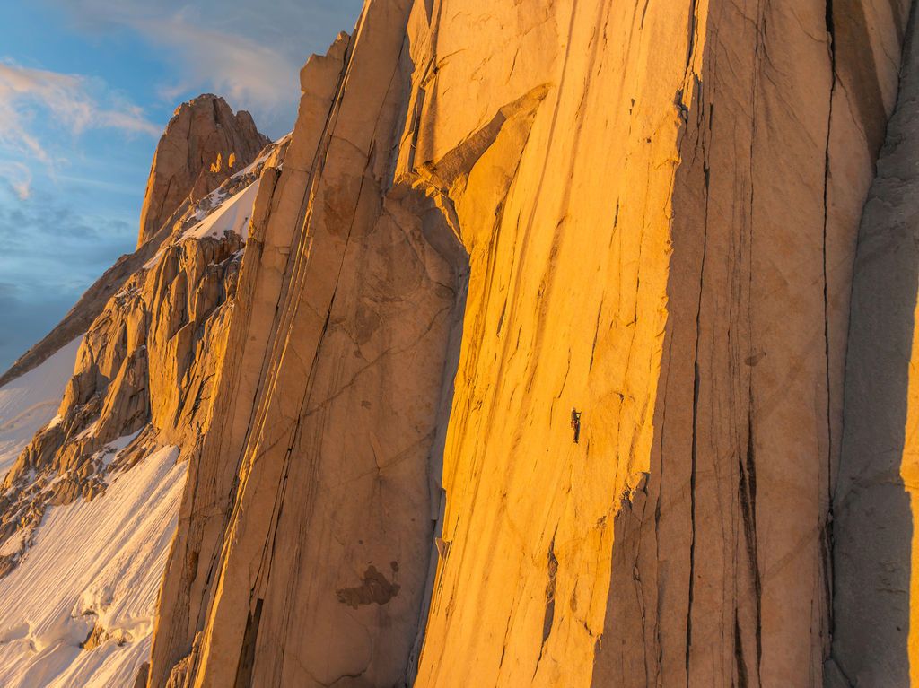 Golden sunset light illuminating a towering granite rock face with climbers visible on the vertical wall.