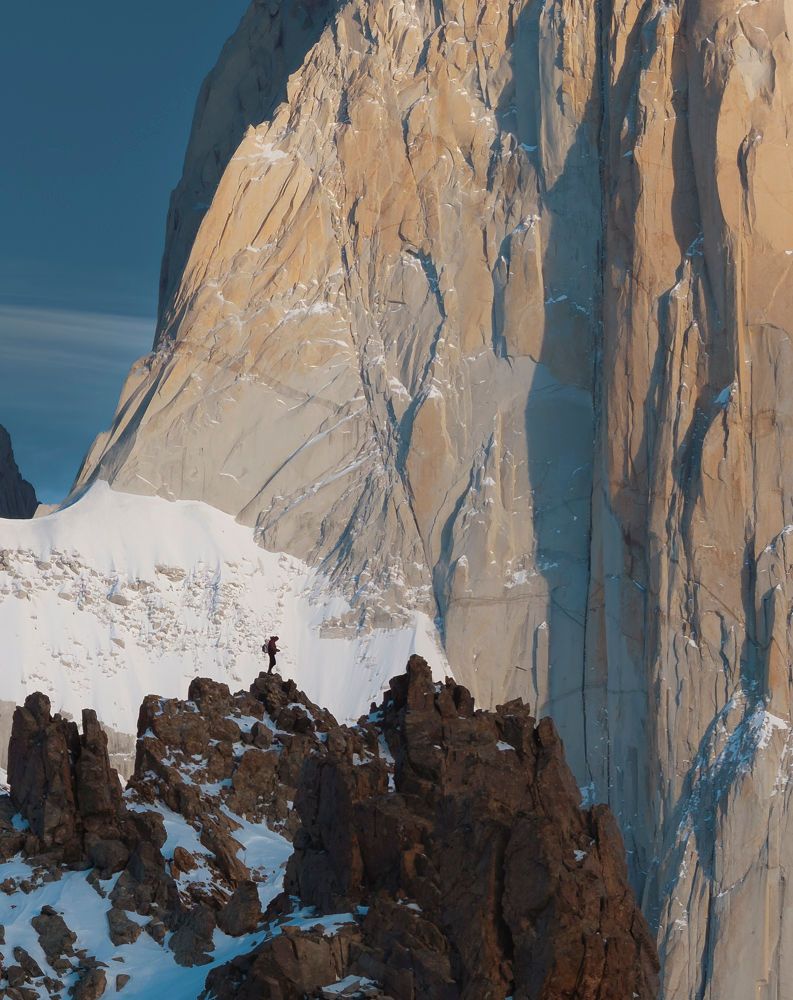 Climber traverses rocky ridge beside the massive sheer granite face of Cerro Torre Patagonia.