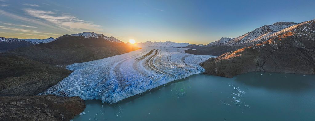 Aerial panoramic view of a glacier flowing into turquoise waters at sunset in Patagonia.