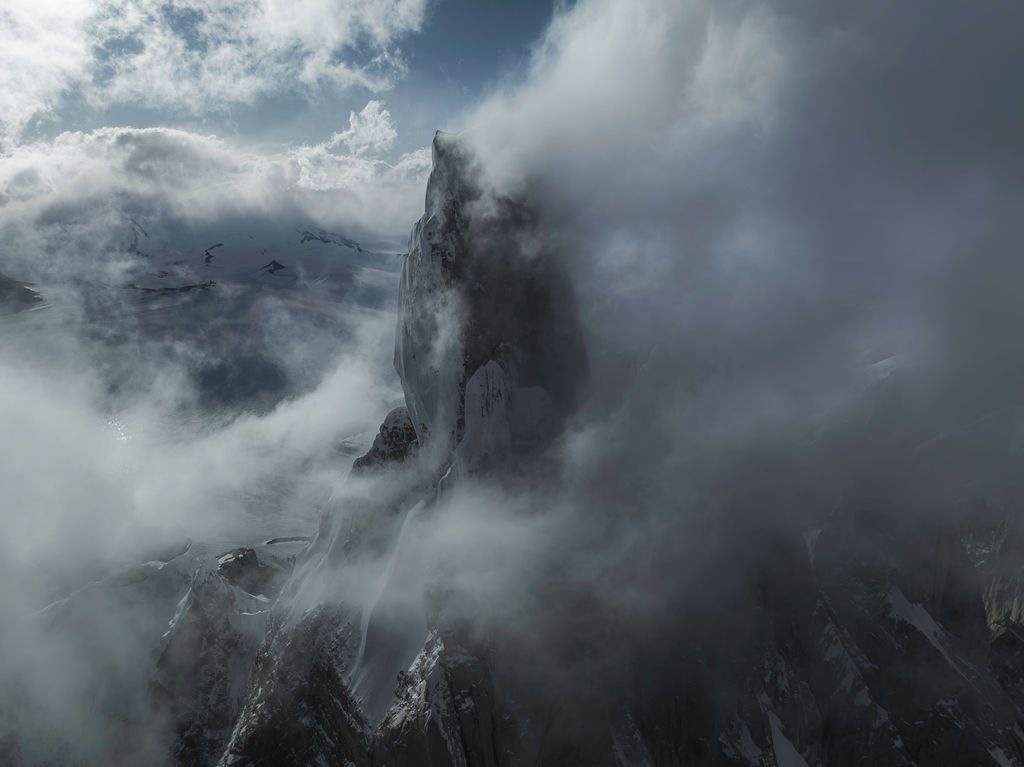 Cerro Torre's iconic granite spire partially obscured by dramatic swirling storm clouds in Patagonia.