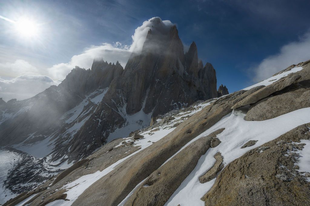 Sunlit rocky mountain spires with snow-covered slopes under a bright blue sky.
