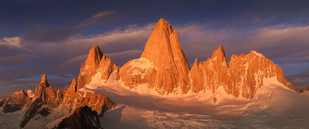 Panoramic view of Mount Fitz Roy and surrounding jagged peaks glowing orange at sunset in Patagonia, Argentina.