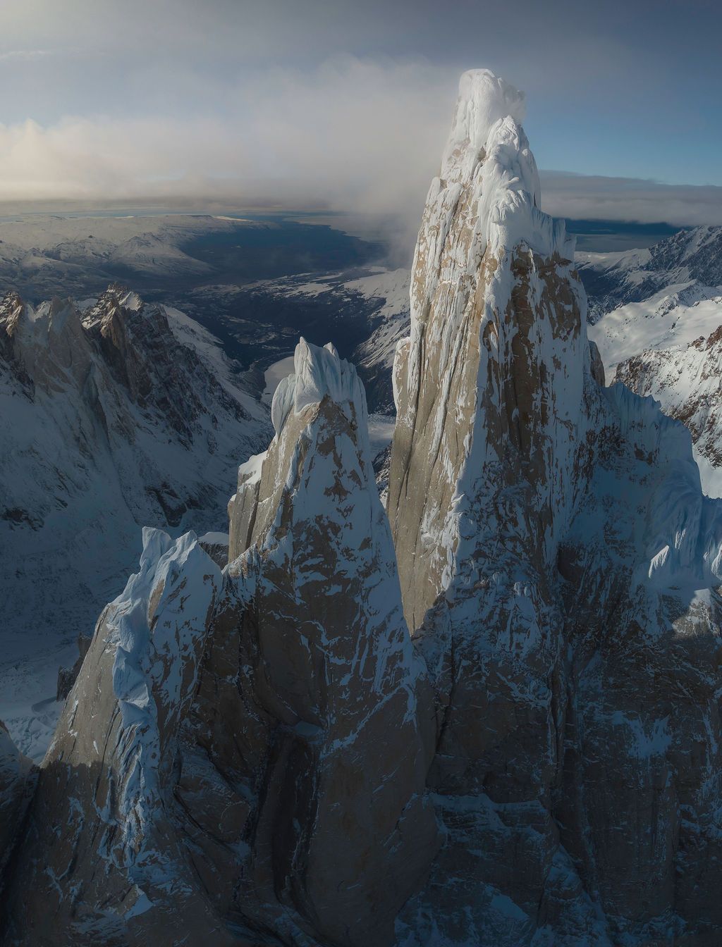 Towering granite spires covered in ice and snow rise above a vast Patagonian mountain valley.