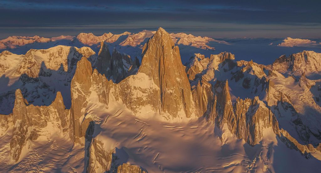 Aerial golden hour view of Cerro Torre's sharp granite spires rising above Patagonian glaciers and snowfields.