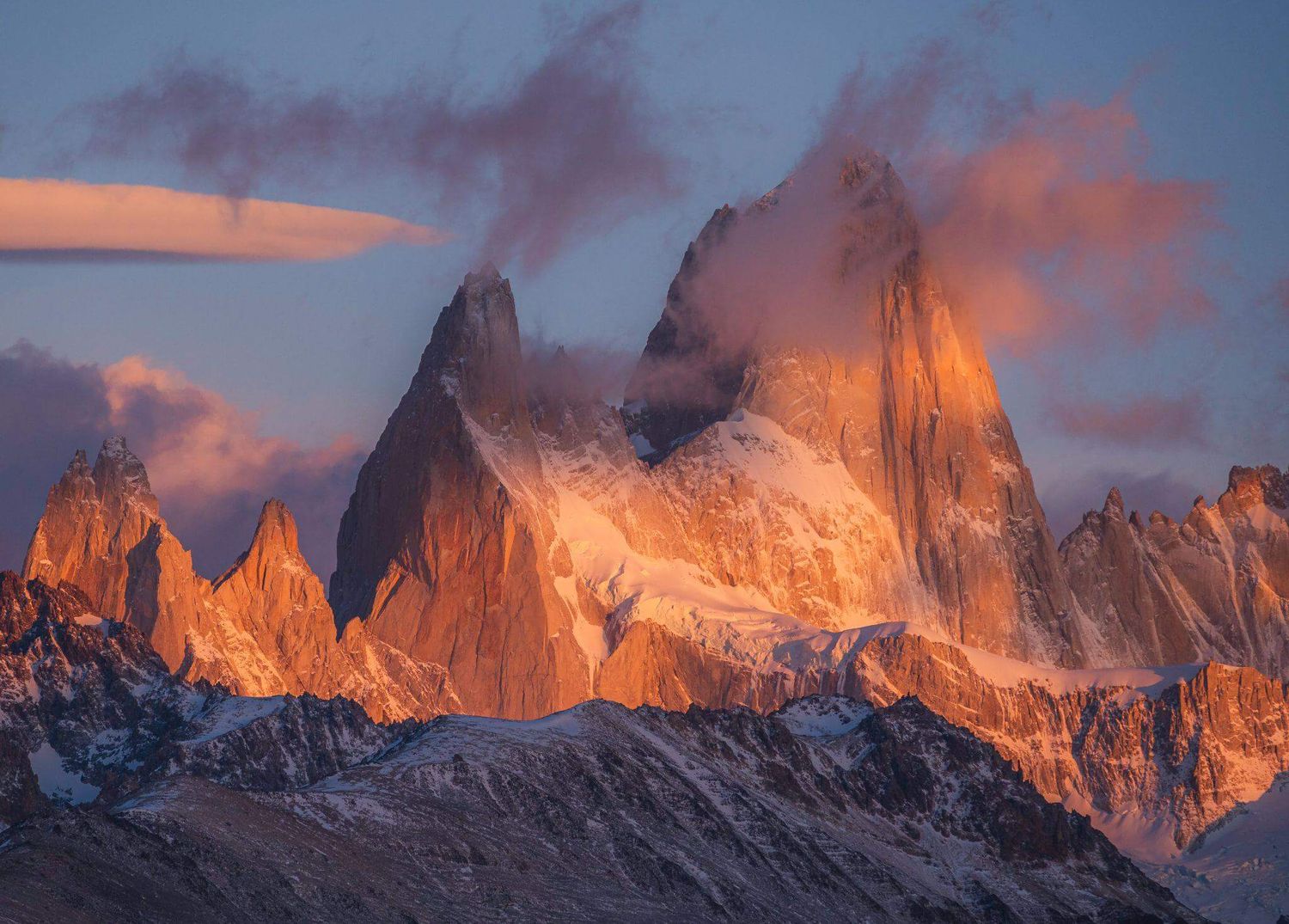 Mount Fitz Roy peaks bathed in warm golden sunset light with dramatic clouds in Patagonia, Argentina.