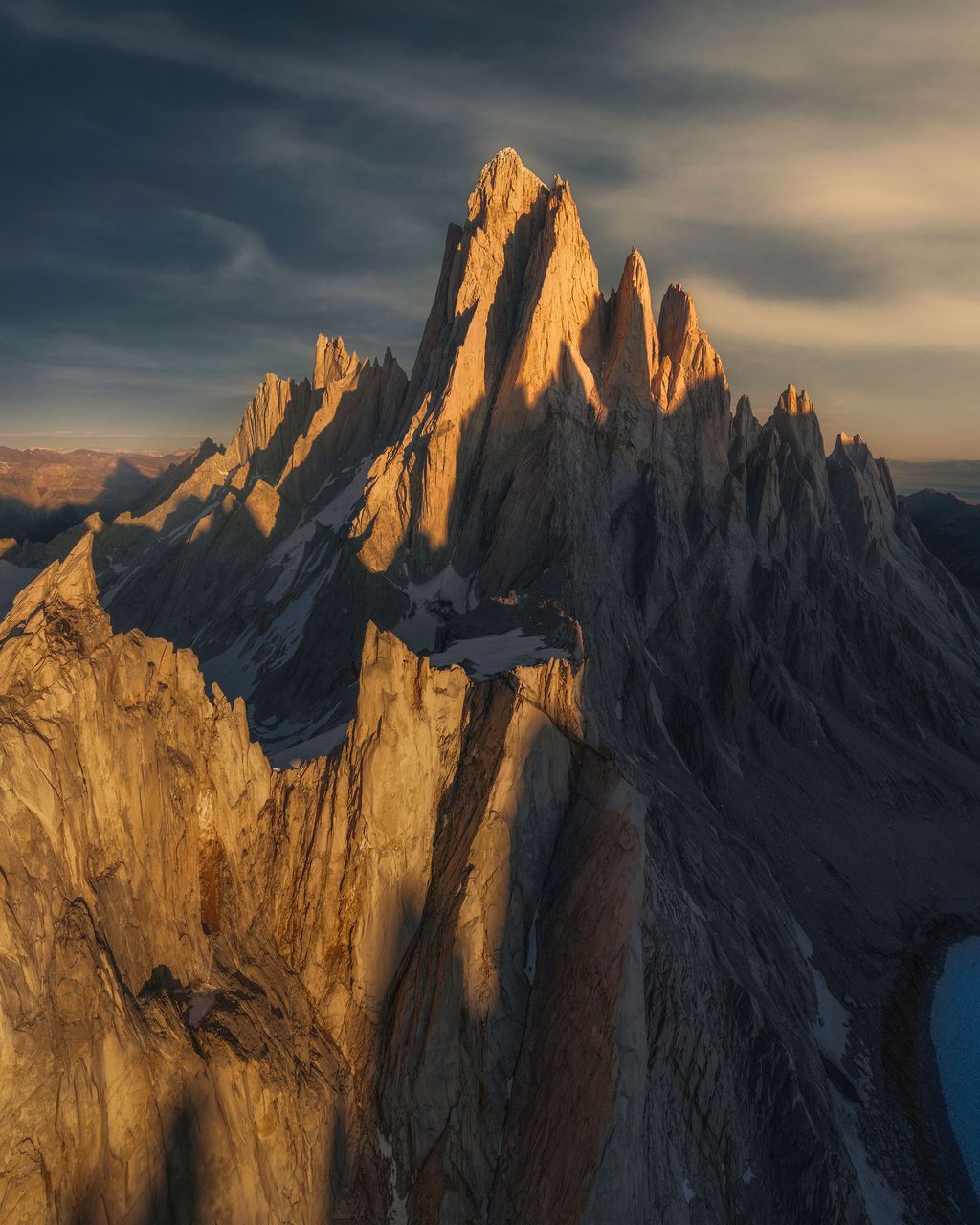 Golden hour aerial view of sharp jagged granite peaks of the Cerro Torre massif glowing under dramatic stormy skies.