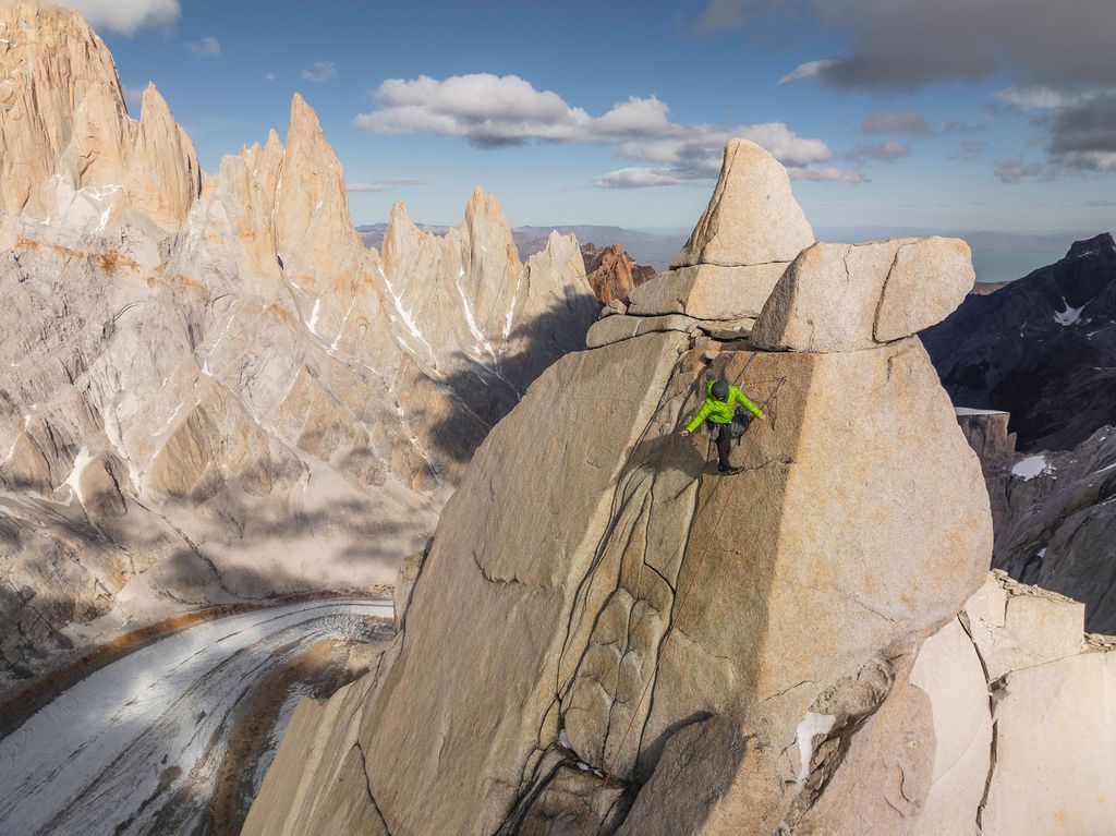 Rock climber scaling a granite face with dramatic Patagonia towers and snow-capped peaks in the background.