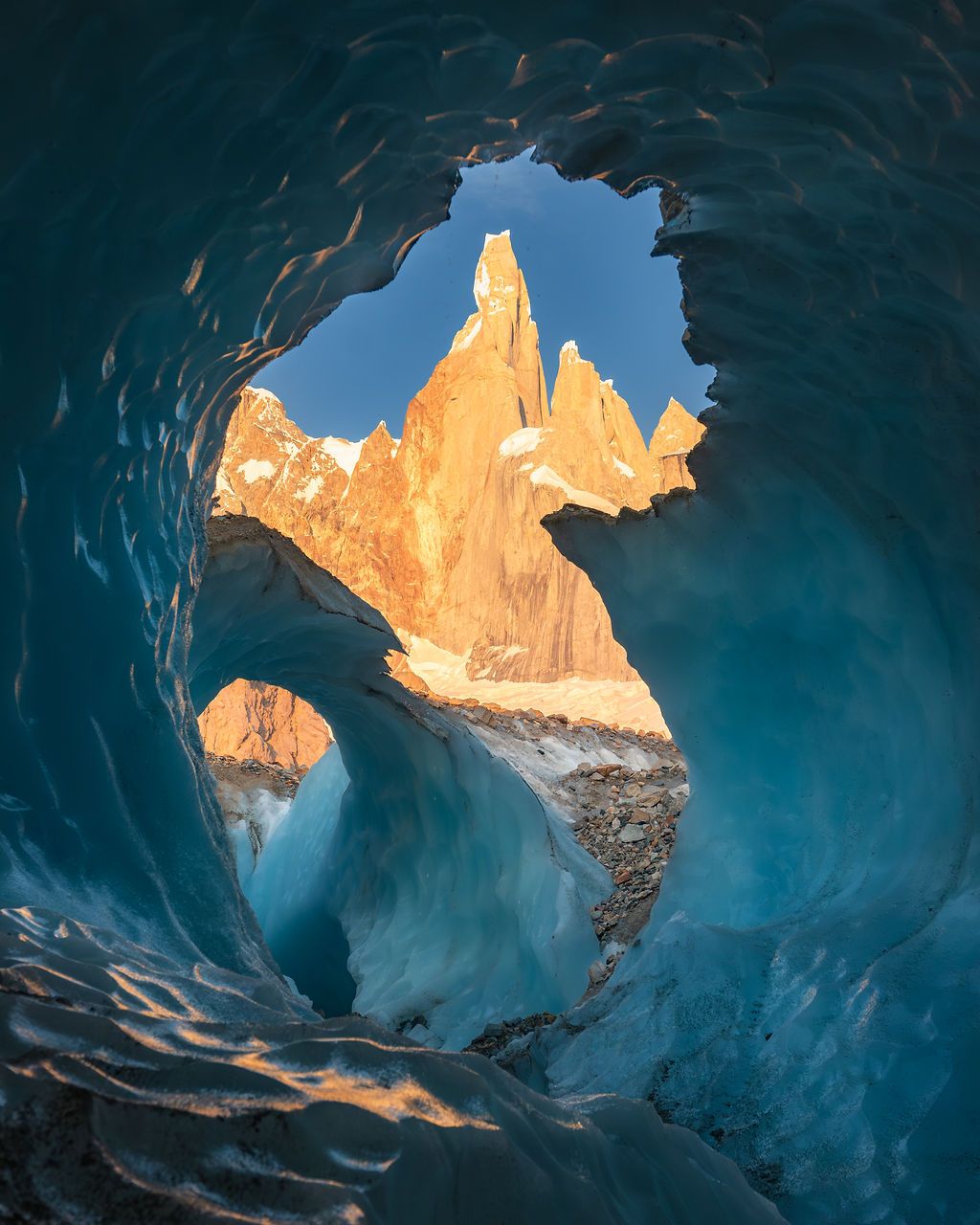 View through a glacial ice cave reveals the golden sunlit spire of Cerro Torre, Patagonia.