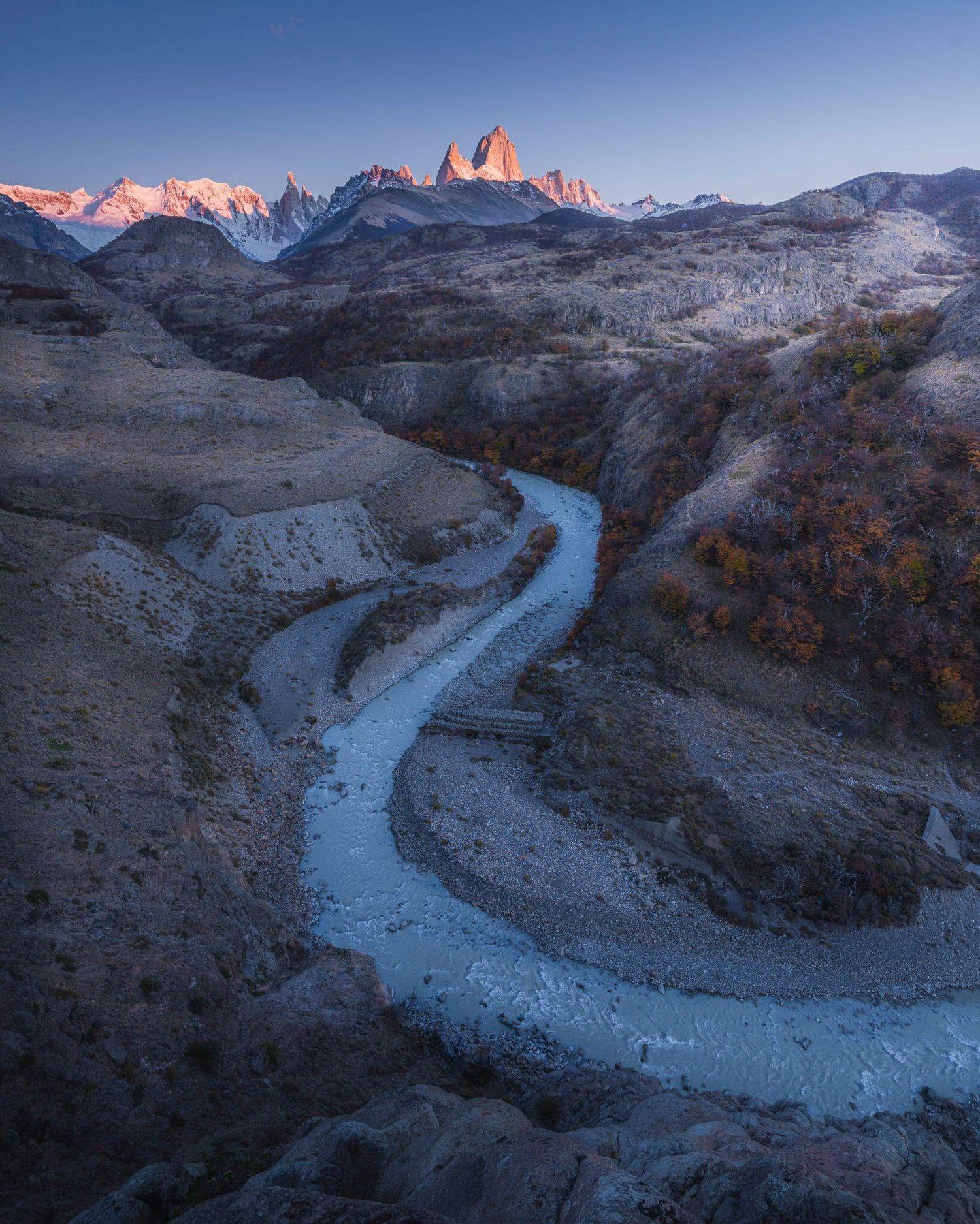 Aerial view of a winding glacial river leading to Mount Fitz Roy at sunset in Patagonia, Argentina.