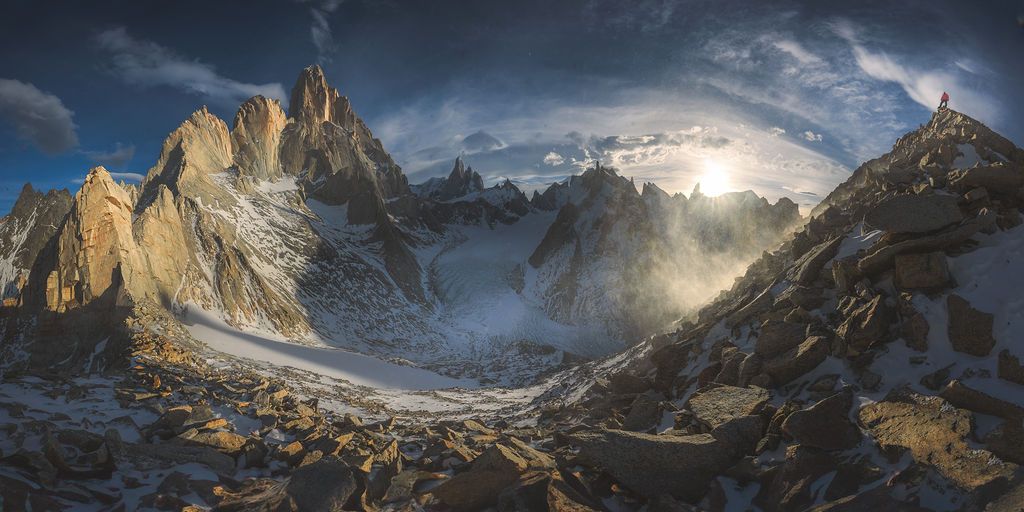 Golden sunlight illuminates dramatic rocky Patagonian mountain peaks with glaciers and swirling mist below.