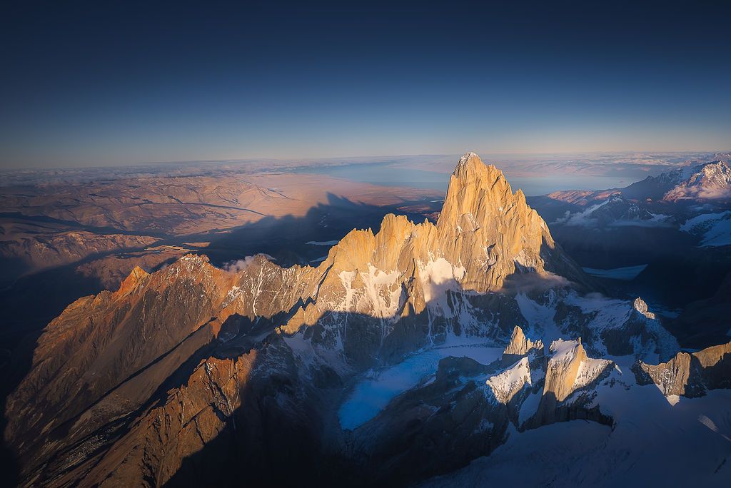 Breathtaking aerial panorama of Mount Fitz Roy rising above snow-covered Patagonian landscape at golden hour.