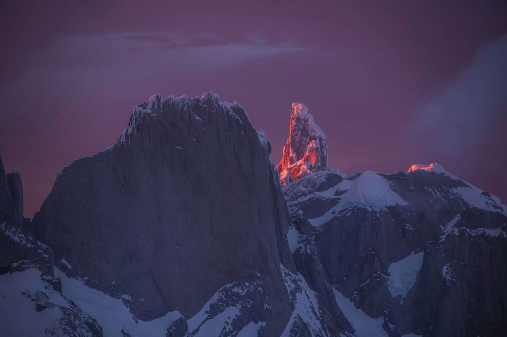 Dramatic crimson alpenglow lights up Cerro Torre peak against a deep purple twilight sky in Patagonia.