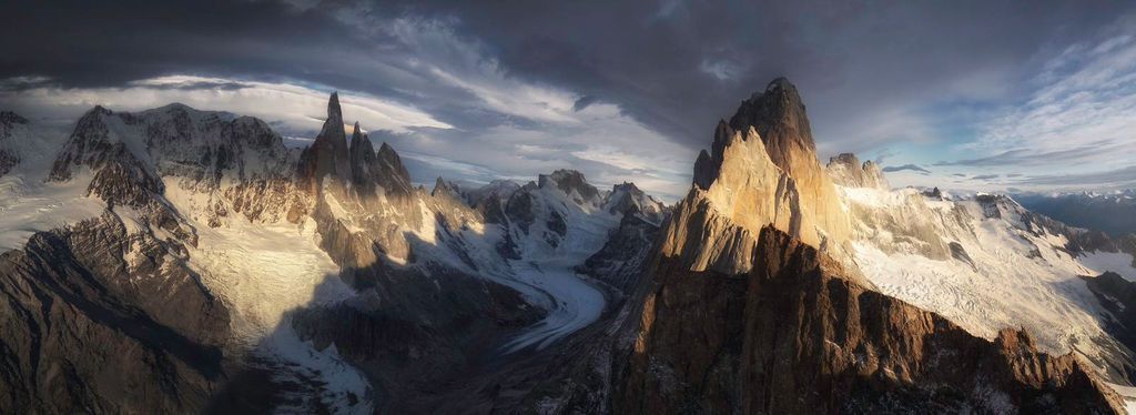 A breathtaking panoramic view of rugged Patagonian mountain peaks with glaciers under dramatic storm clouds.