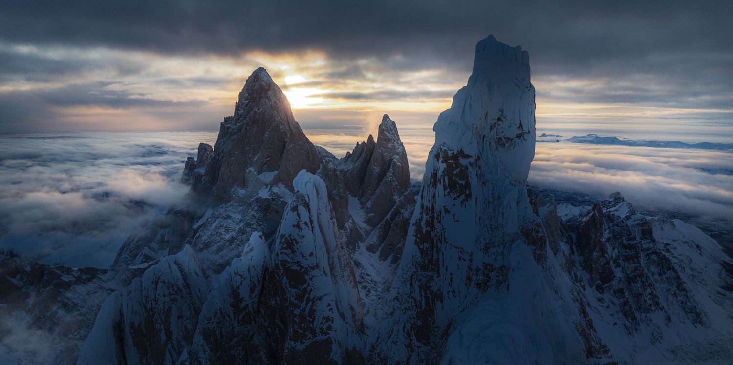 Snow-capped jagged mountain peaks rise above clouds at dramatic sunset in the Dolomites, Italy.