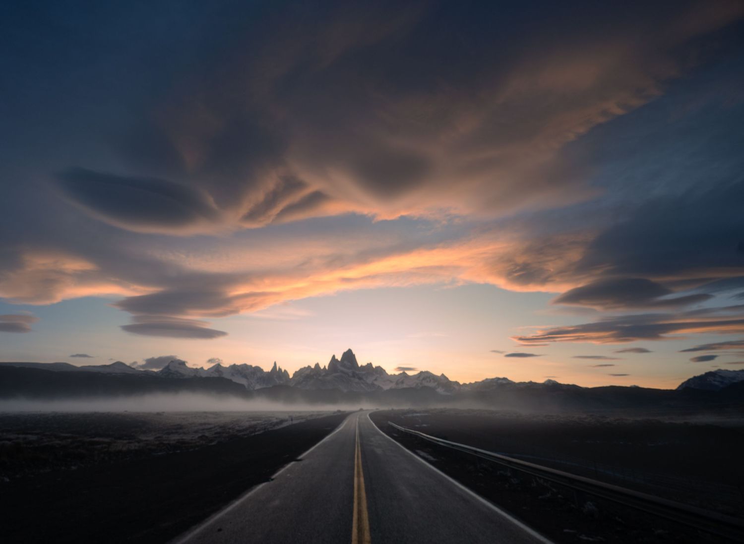 A dramatic road stretching toward misty mountains under a vivid sunset sky with swirling clouds in Patagonia.