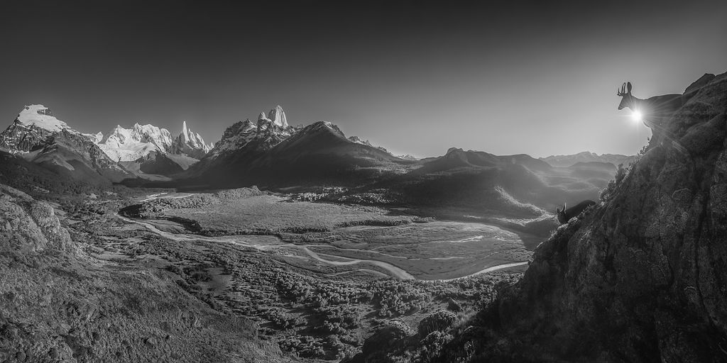 Black and white panorama of Patagonian valley with hiker on rocky cliff under moonlight.
