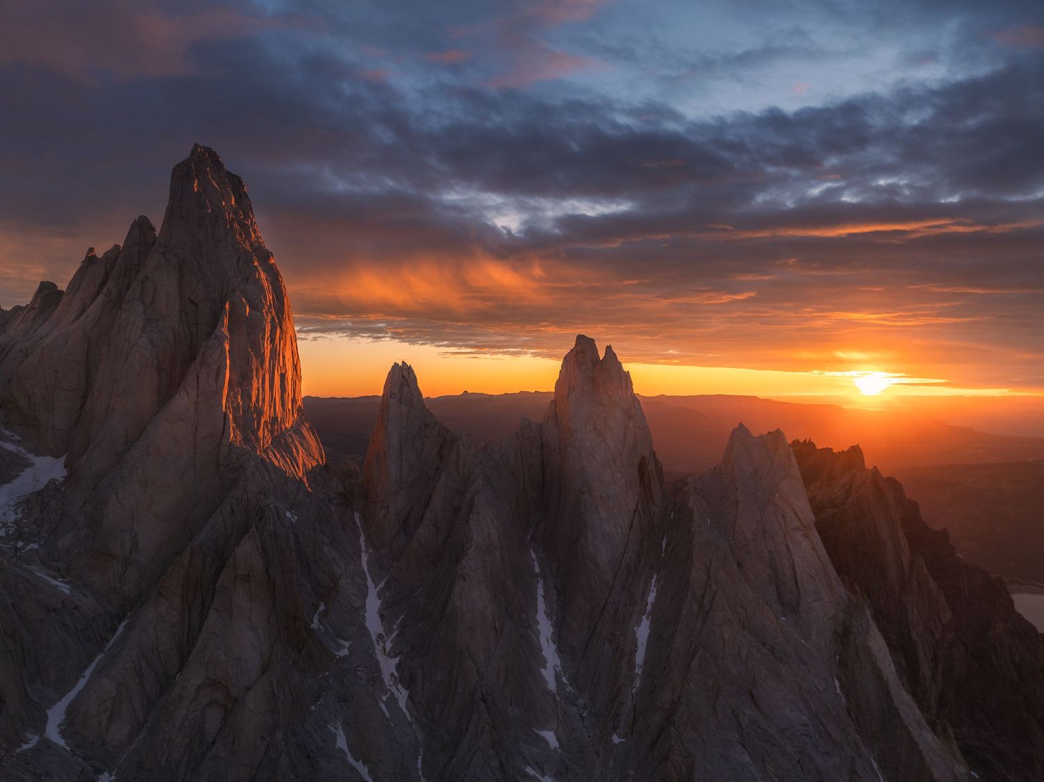 Dramatic sunset over jagged mountain peaks in the Dolomites, with vivid orange and red sky illuminating rocky spires.