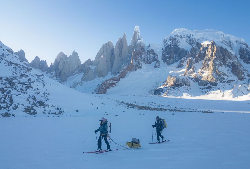 Two skiers crossing a snowy glacier with dramatic Patagonian mountain peaks in the background.