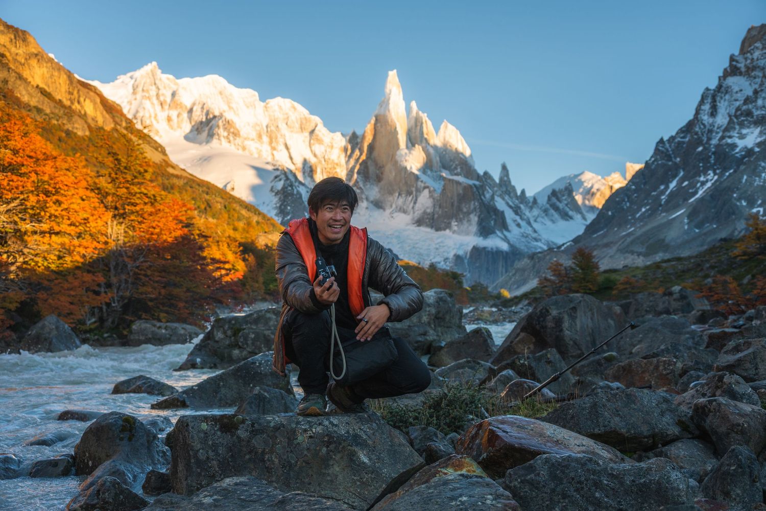 Hiker crouching on rocks with stunning Cerro Torre mountain peaks and autumn foliage in Patagonia, Argentina.