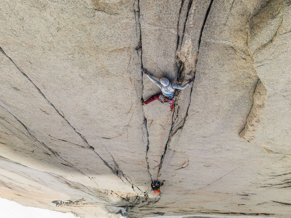 Rock climber navigates a crack system on an overhanging granite slab with a second climber belaying below.