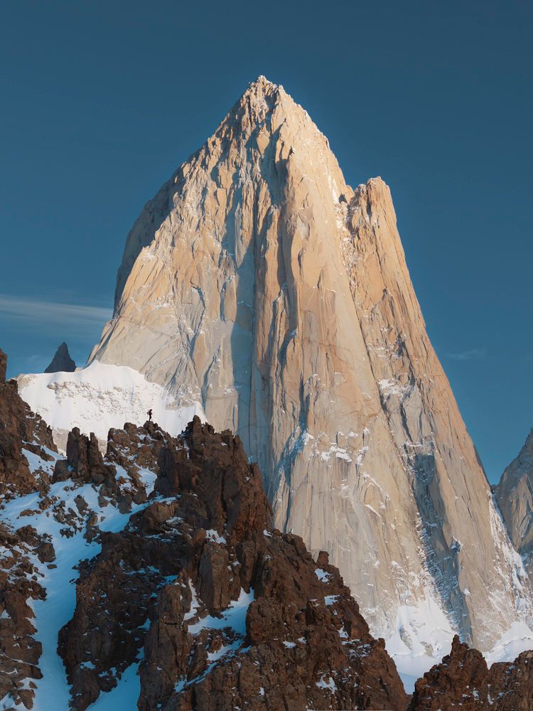 Towering granite spire of Mount Fitz Roy glowing in warm morning light against a clear blue sky in Patagonia.