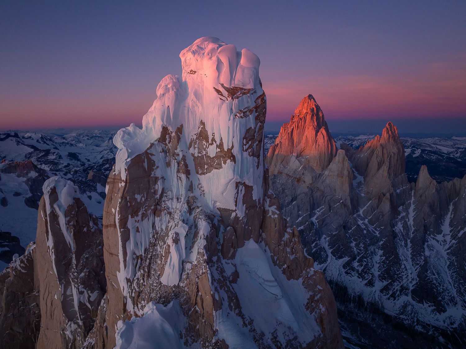 Snow-capped jagged mountain peaks glow in pink and orange alpenglow at sunrise in Patagonia.