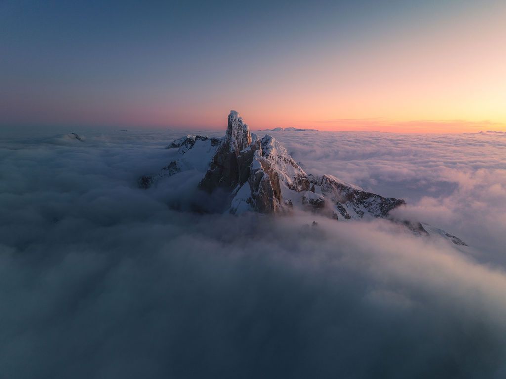 Snow-capped mountain peak pierces through a dramatic sea of clouds at colorful twilight in Patagonia.