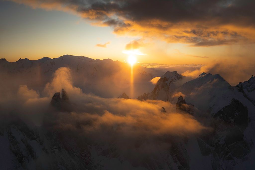 Golden sunset bursting through dramatic clouds over snow-capped mountain peaks in a breathtaking alpine landscape.