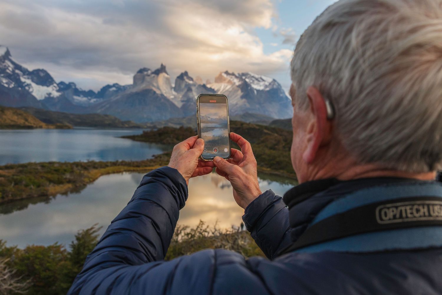 Person photographing stunning Torres del Paine mountain peaks and lake landscape in Patagonia, Chile on a smartphone.