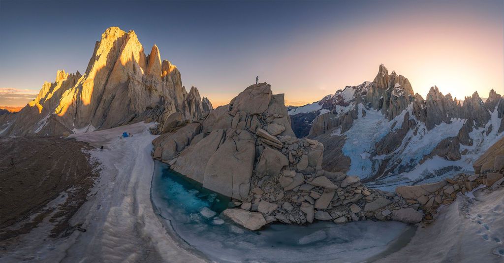 Aerial panorama of Cerro Torre massif with frozen glacial lake at golden hour in Patagonia.