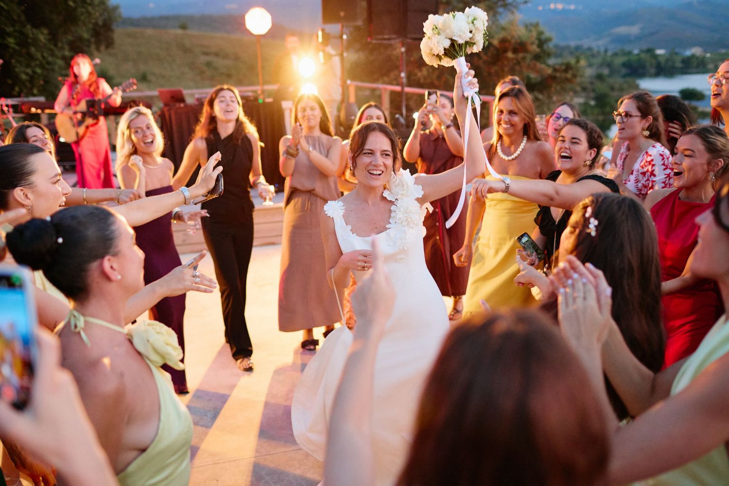 Joyful bride celebrated by guests during energetic wedding bouquet toss ceremony.