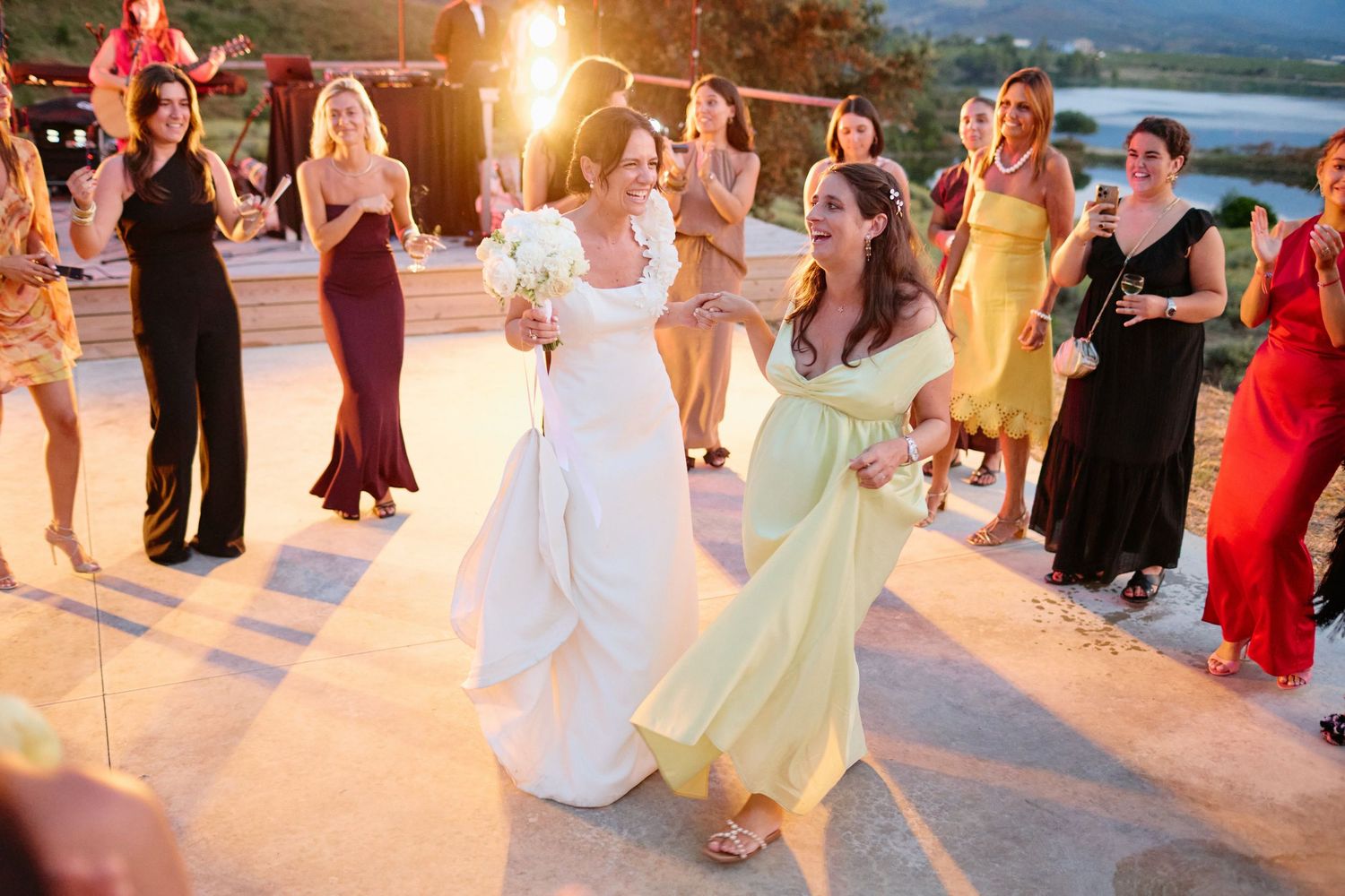 Bride dancing with guests at outdoor wedding reception with sparklers at sunset.