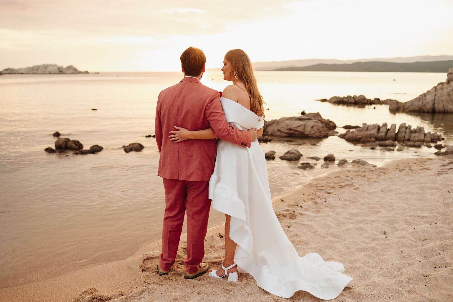 Bride and groom standing together gazing at scenic ocean view during beach sunset wedding.