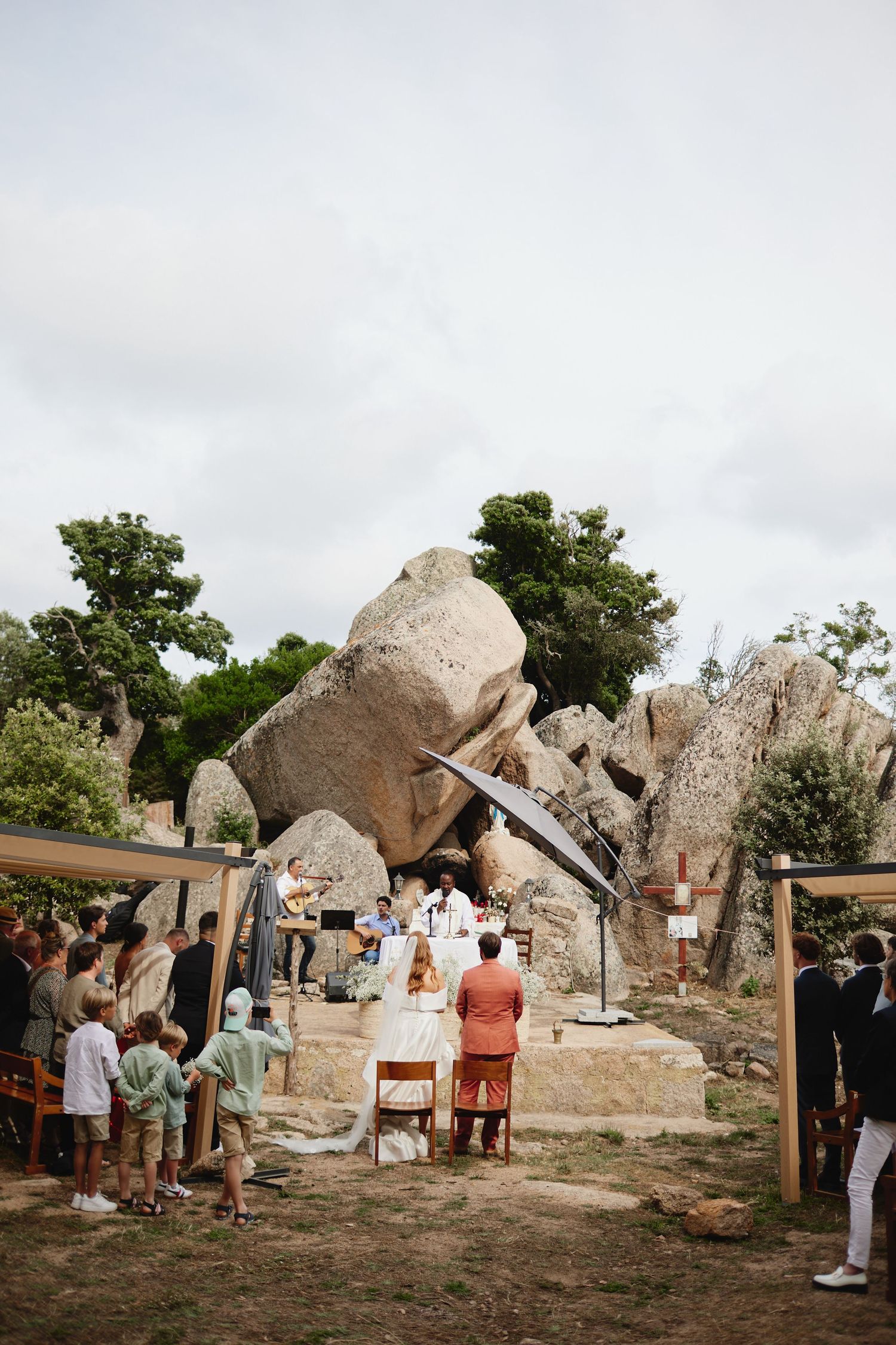 Outdoor wedding ceremony set against dramatic large granite boulders with guests seated and couple at altar.