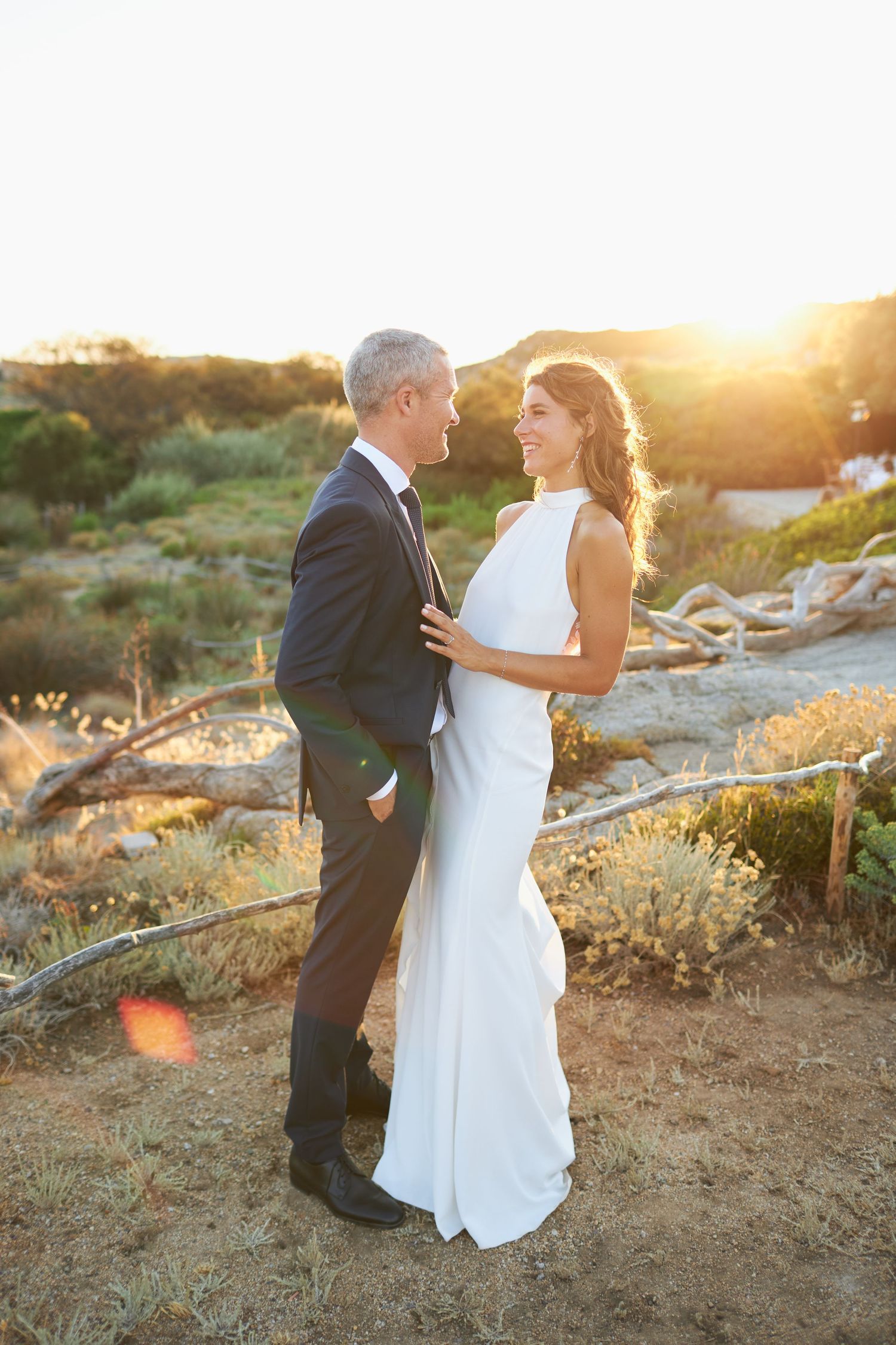 Bride and groom embrace at golden hour sunset in a scenic outdoor desert landscape.
