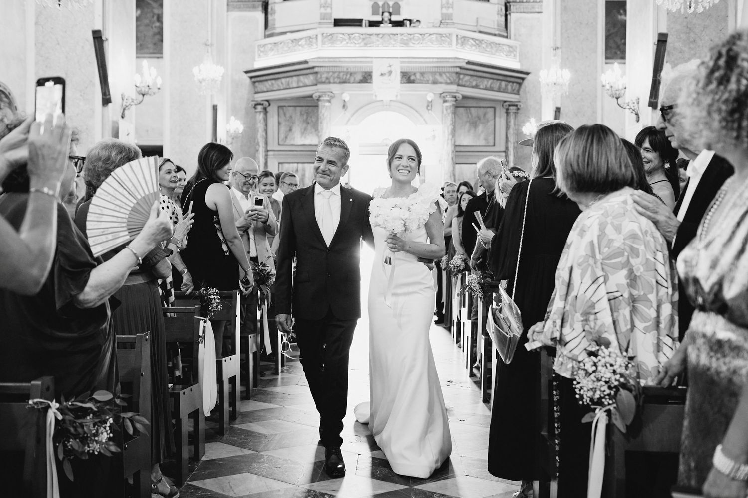 Newlyweds walk down church aisle in black and white wedding ceremony photo.