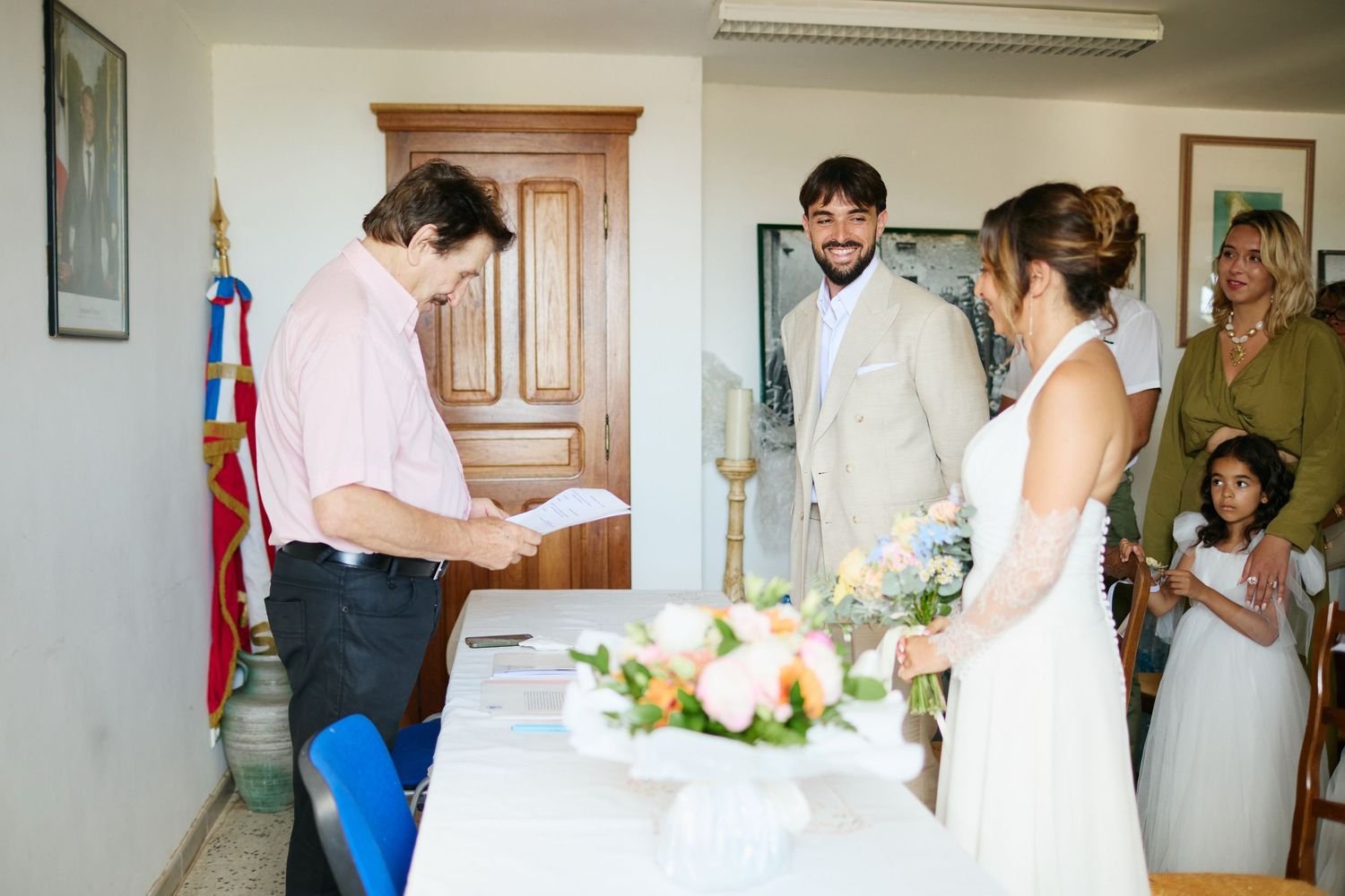 Officiant reads vows to smiling bride and groom during an intimate civil wedding ceremony indoors.