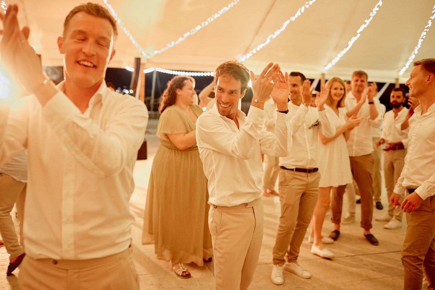 Wedding guests dancing energetically on the dance floor under fairy lights in a beautifully decorated tent.