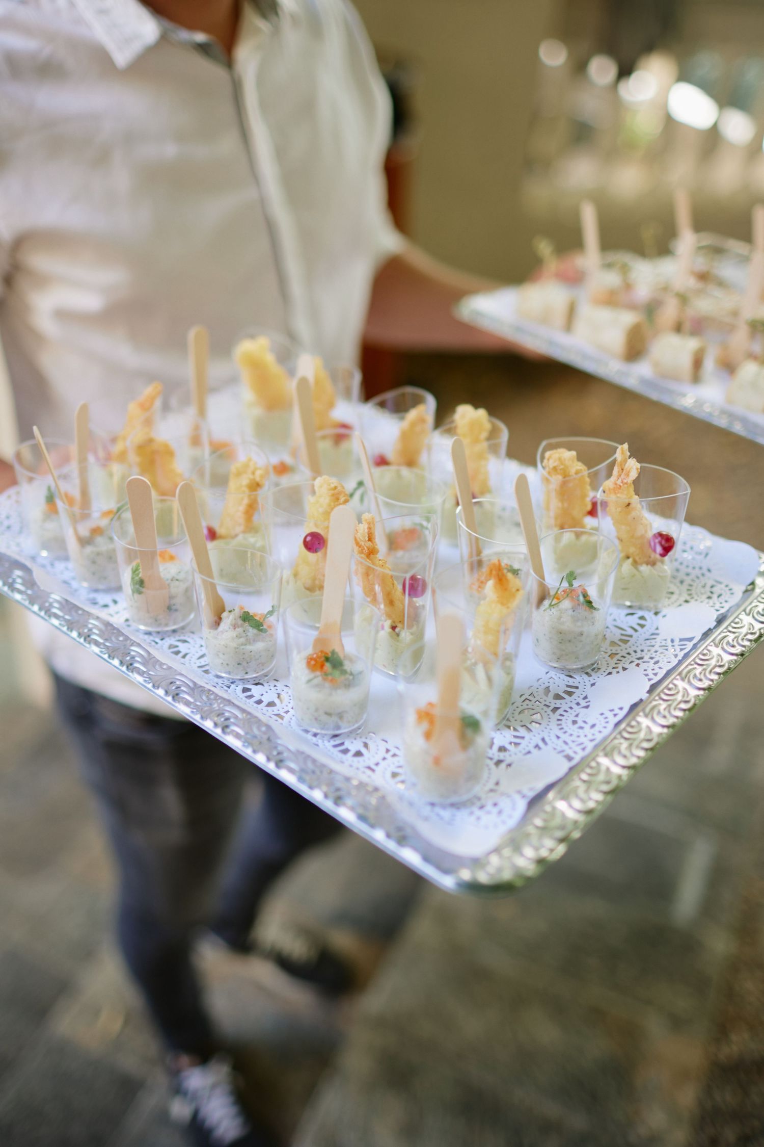 Close-up of elegant wedding canapés served in small glasses on silver tray.