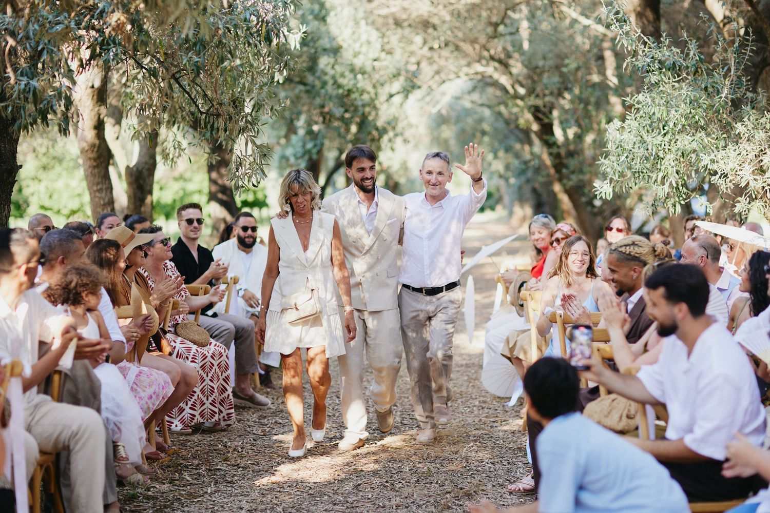 Joyful newlyweds and family walk back down the aisle after their outdoor olive grove wedding ceremony.