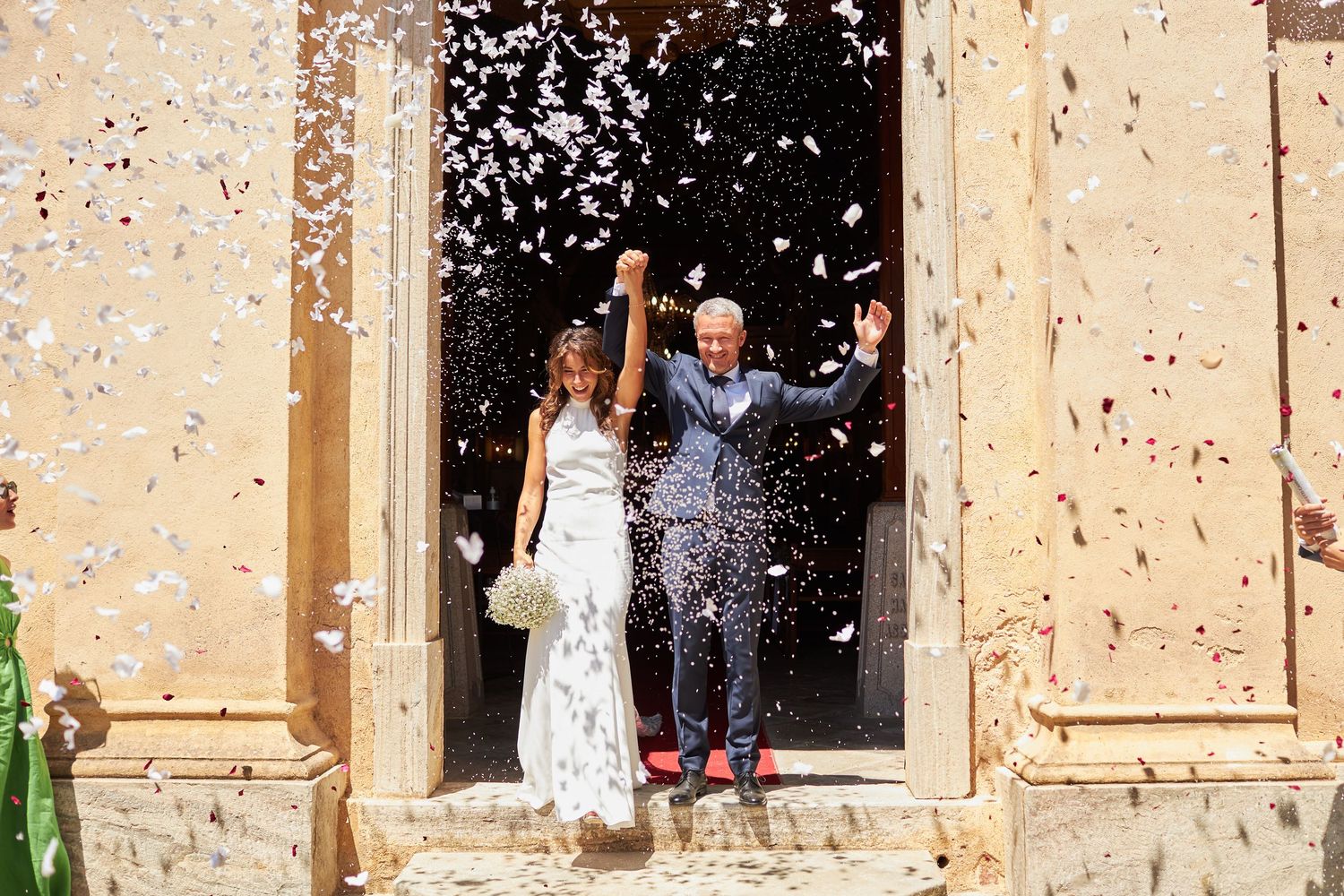 Bride and groom exit church doors in confetti shower, celebrating after their wedding ceremony.