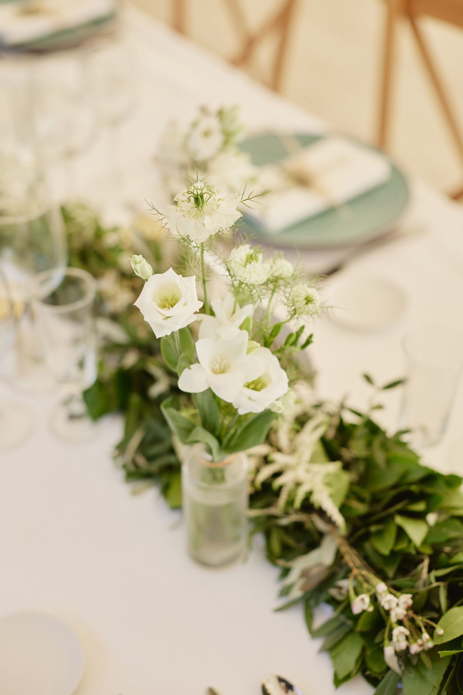 Elegant wedding table centerpiece with white lisianthus flowers and lush green garland runner.