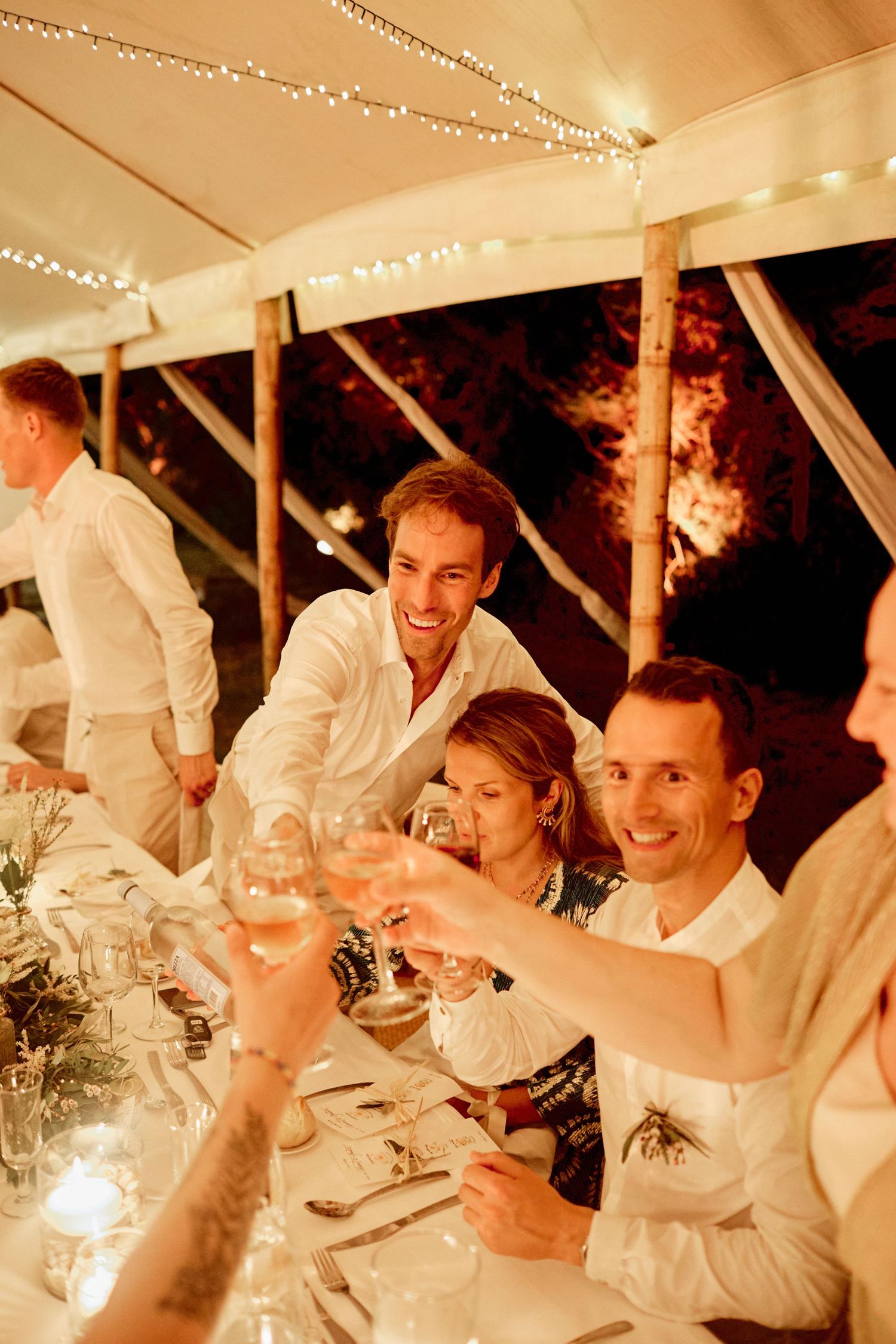 Wedding guests raising champagne glasses in a toast at an elegantly decorated candlelit reception table.