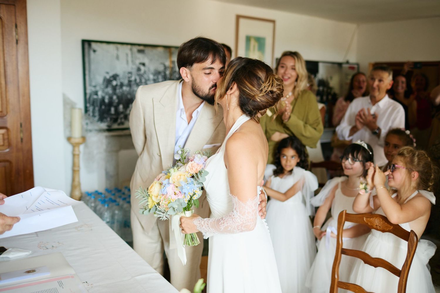 Bride and groom share first kiss at wedding ceremony while guests watch joyfully.