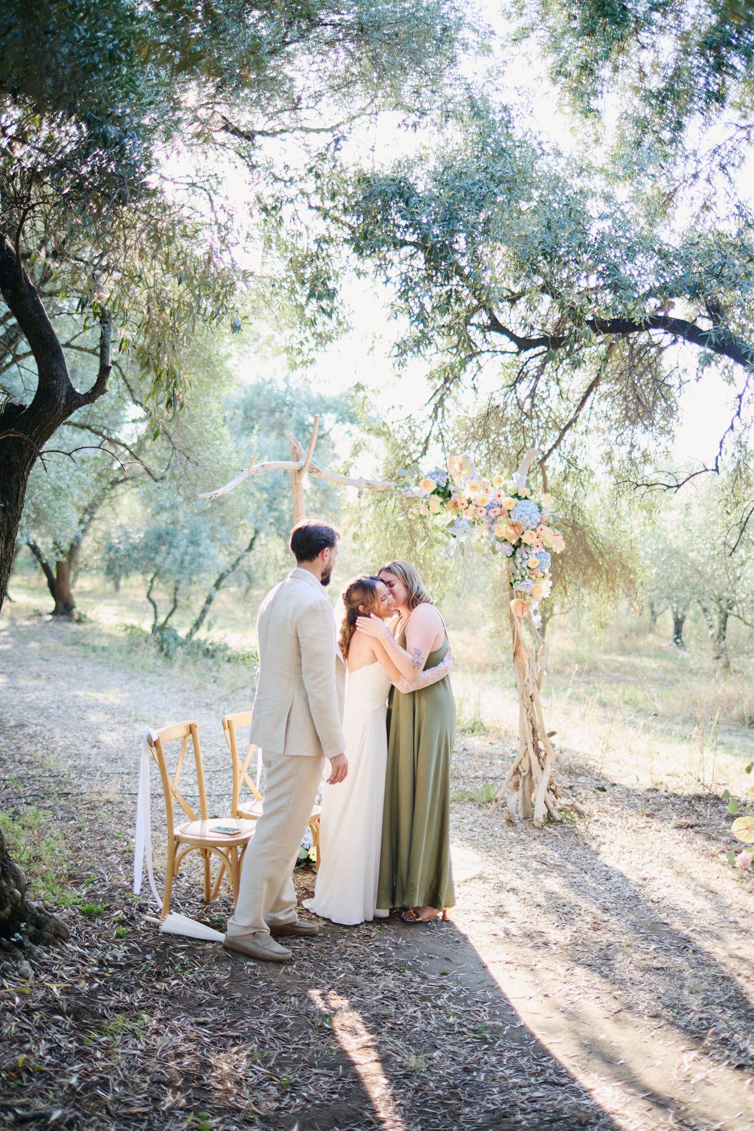 Bride and groom sharing an embrace with their officiant after an outdoor woodland wedding ceremony.