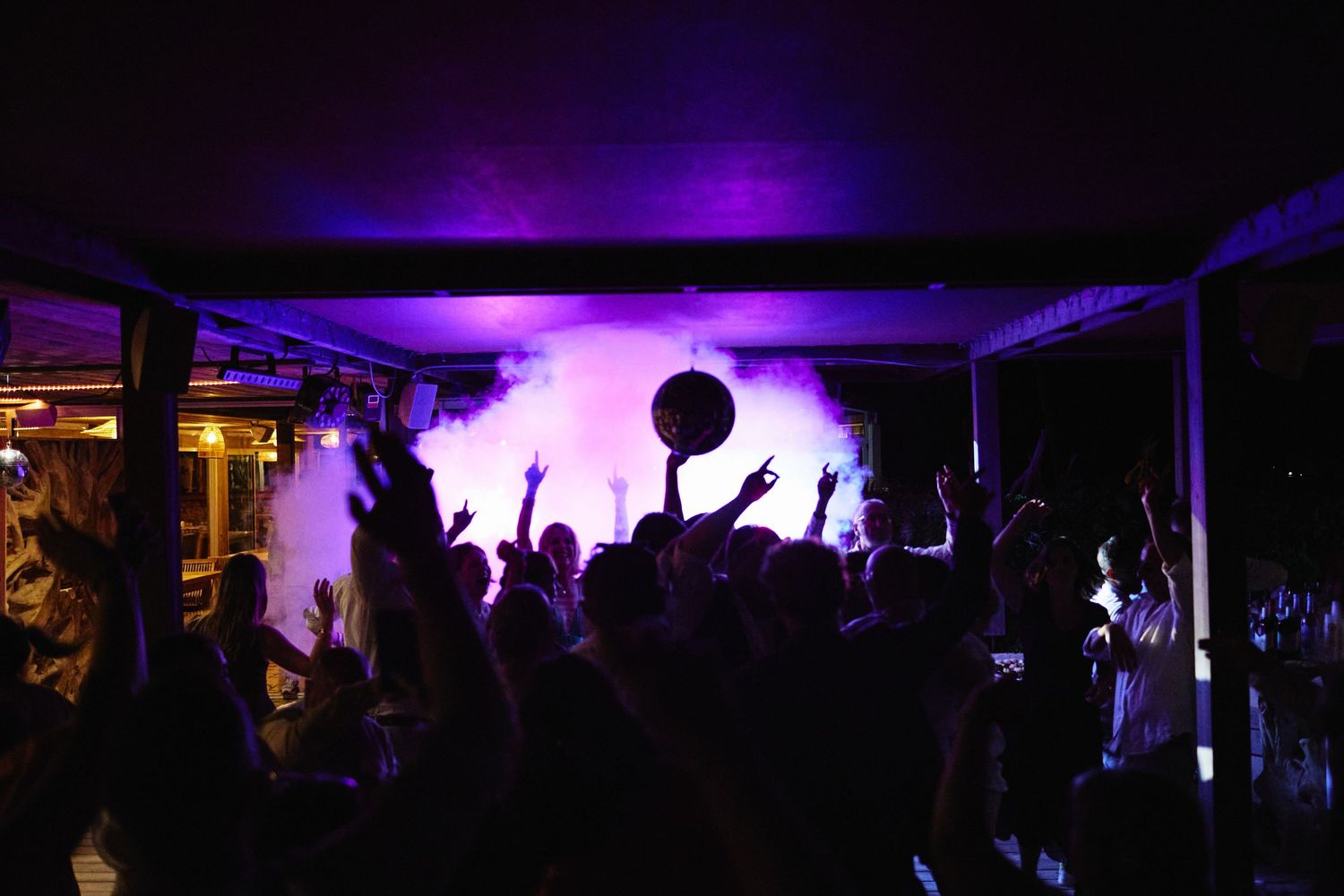 Crowd of wedding guests dancing in purple smoke and dramatic lighting at late night reception.