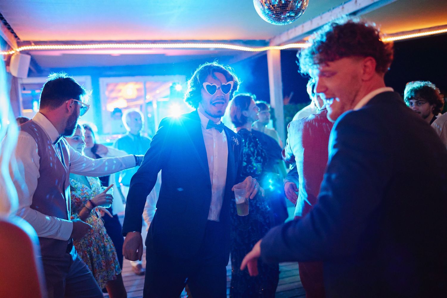 Young men dancing energetically under blue neon lights at a stylish evening wedding party.