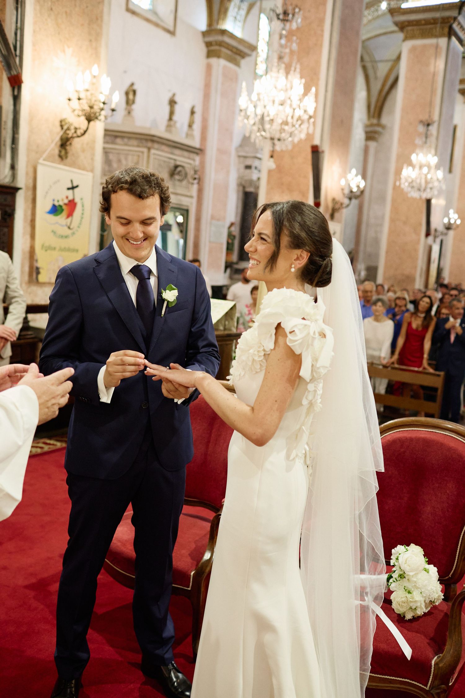 Groom placing wedding ring on brides finger at ornate church altar during ceremony.