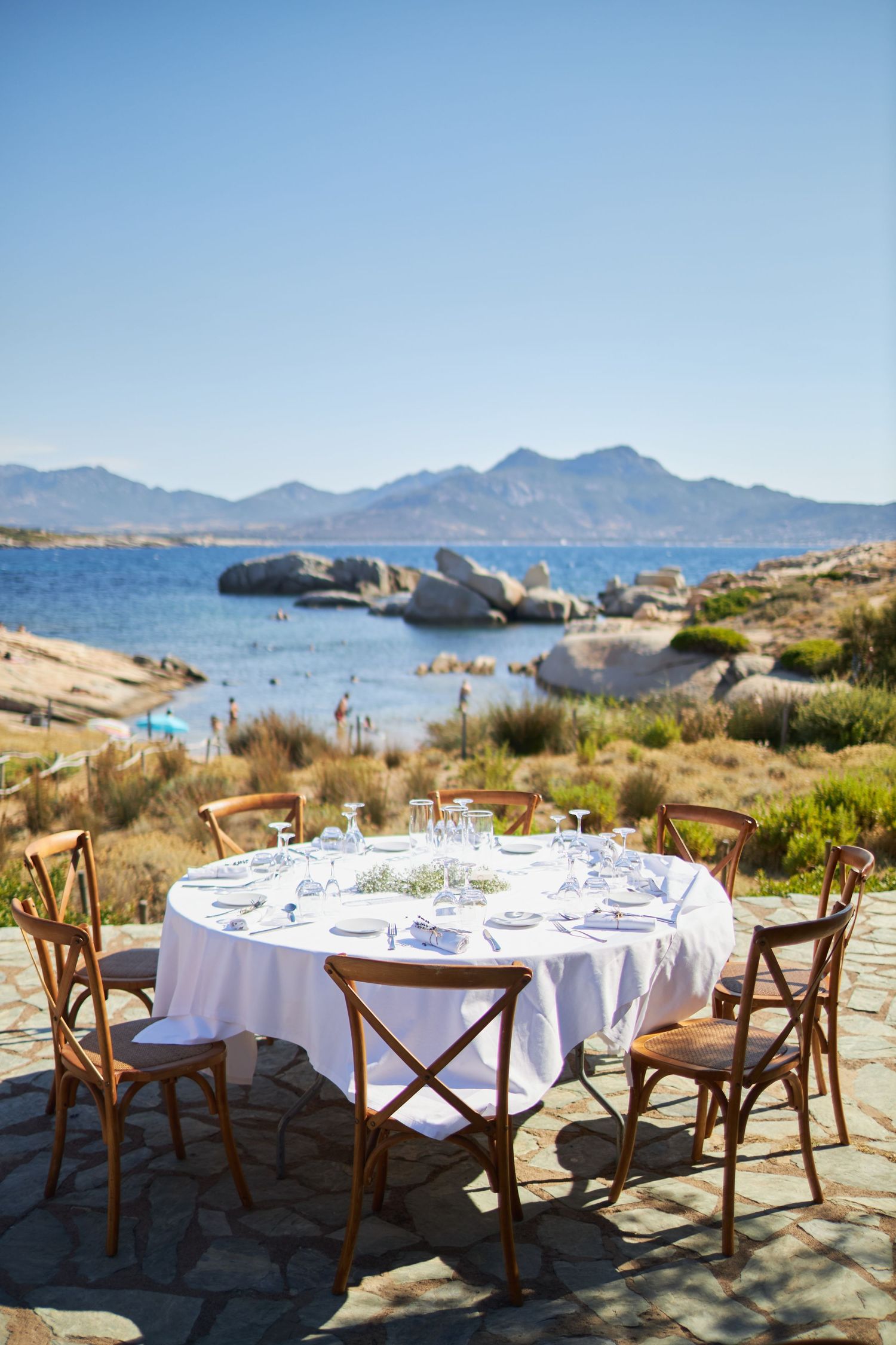 Round outdoor wedding reception table set with white linen overlooking scenic coastal Mediterranean view.