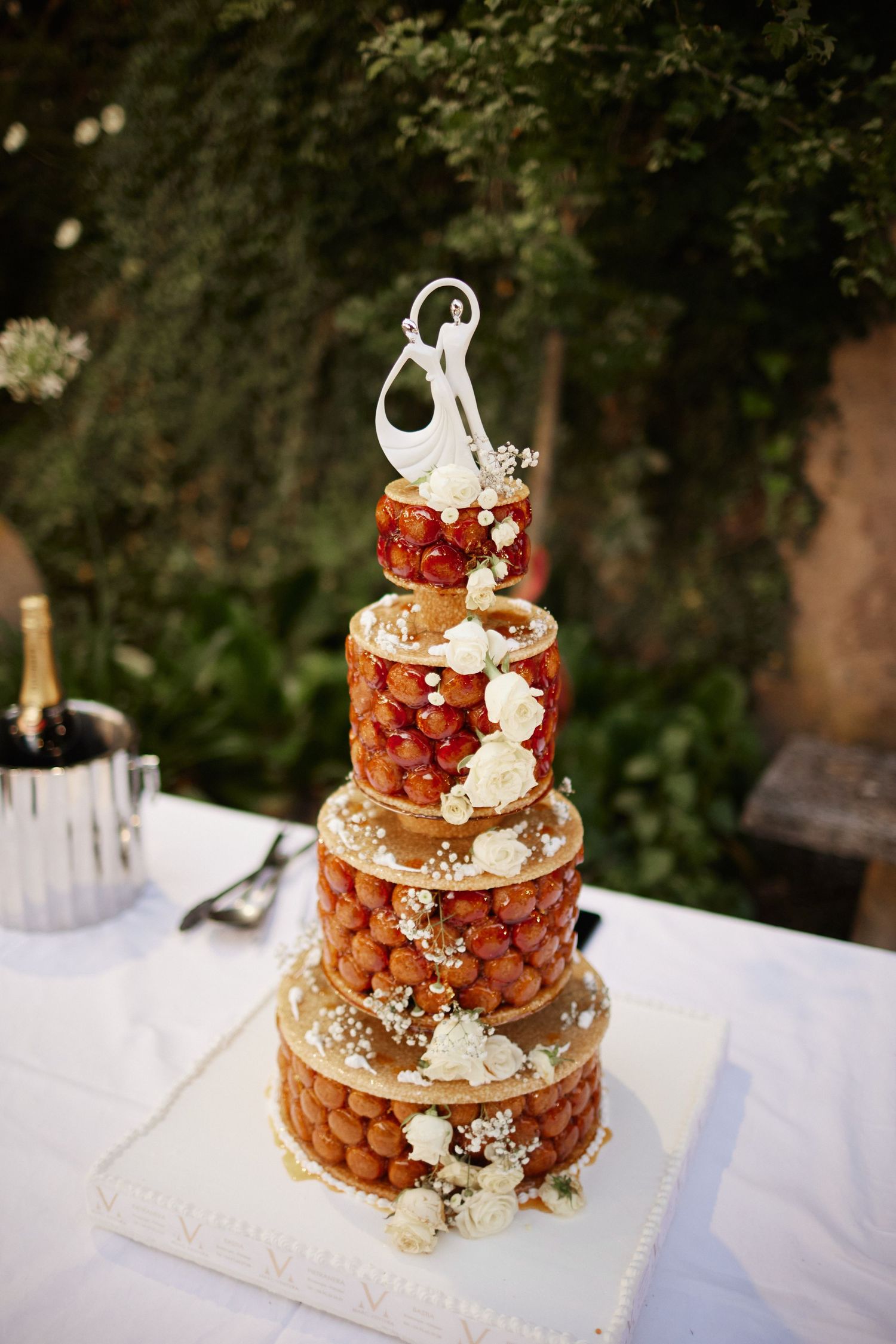 Elegant croquembouche wedding cake topped with dancing couple figurine, decorated with white roses and berries.